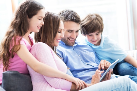 a family sitting on a couch together looking at a tablet being held by the father