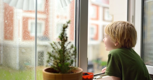 little boy looking out rainy window