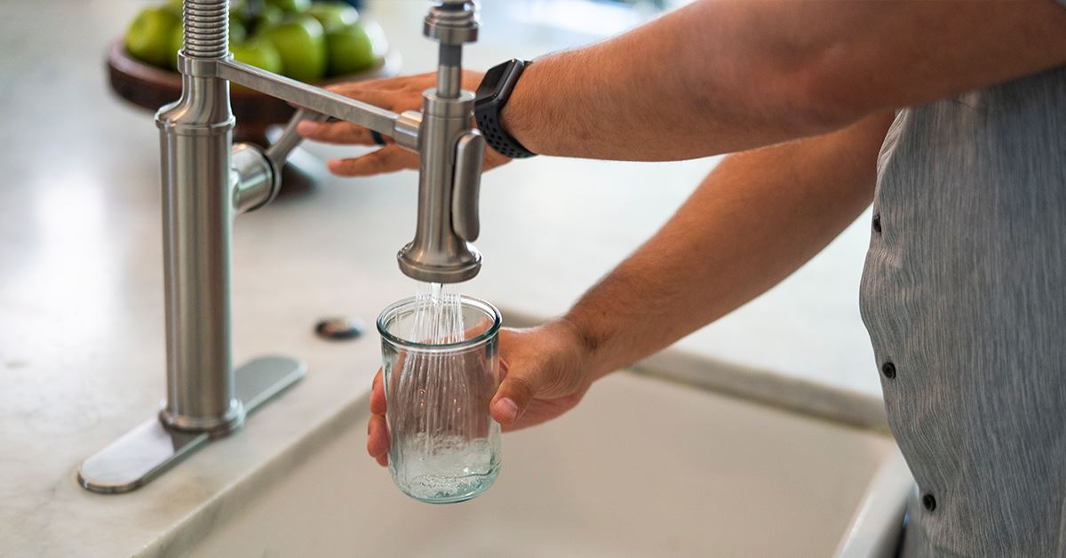 person filling cup of water from faucet