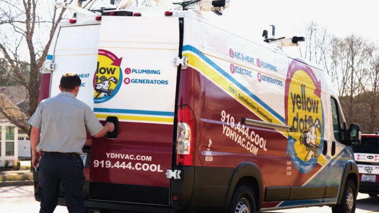 A technician opens the back door of a Yellow Dot service van parked outdoors. The van displays HVAC, plumbing, electric, and generator services and contact details.